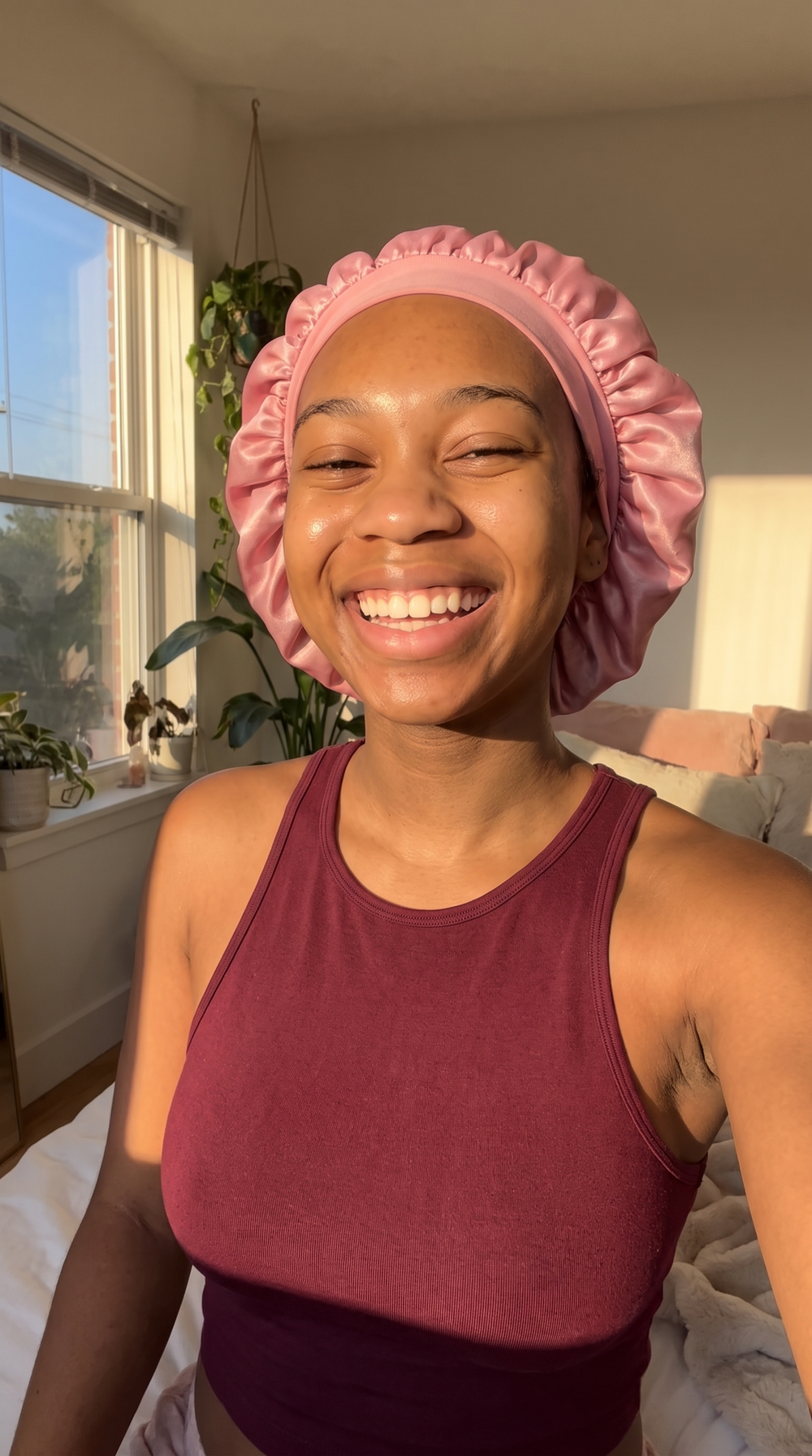Smiling woman in a satin bonnet with clear, even-toned skin in golden sunlight